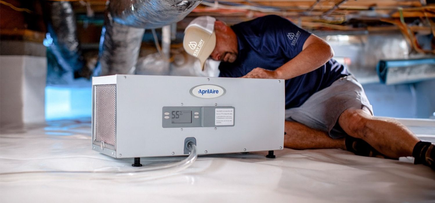 A technician installs a dehumidifier in a sealed crawl space as part of a basement waterproofing and moisture control system.
