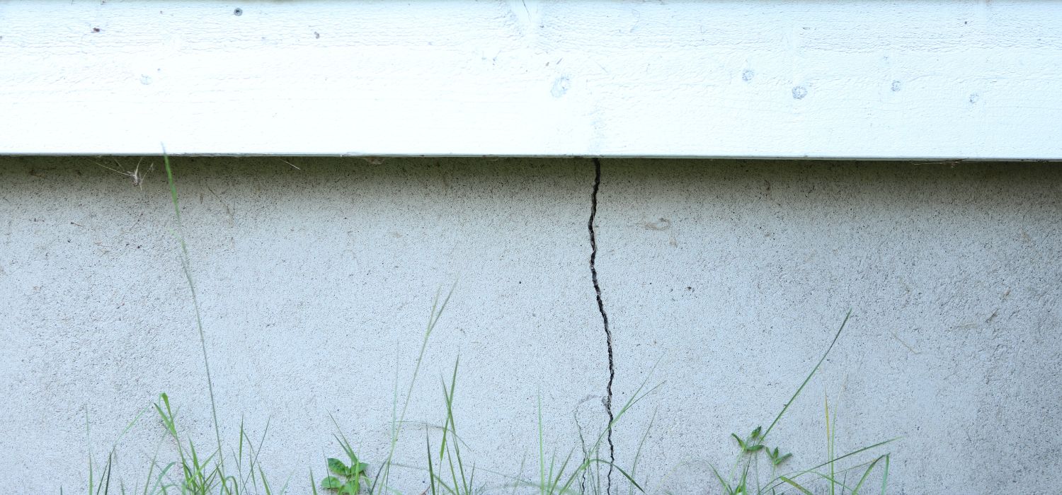 Vertical crack in a home’s concrete foundation wall near ground level, showing a common sign of structural or settlement-related foundation damage.